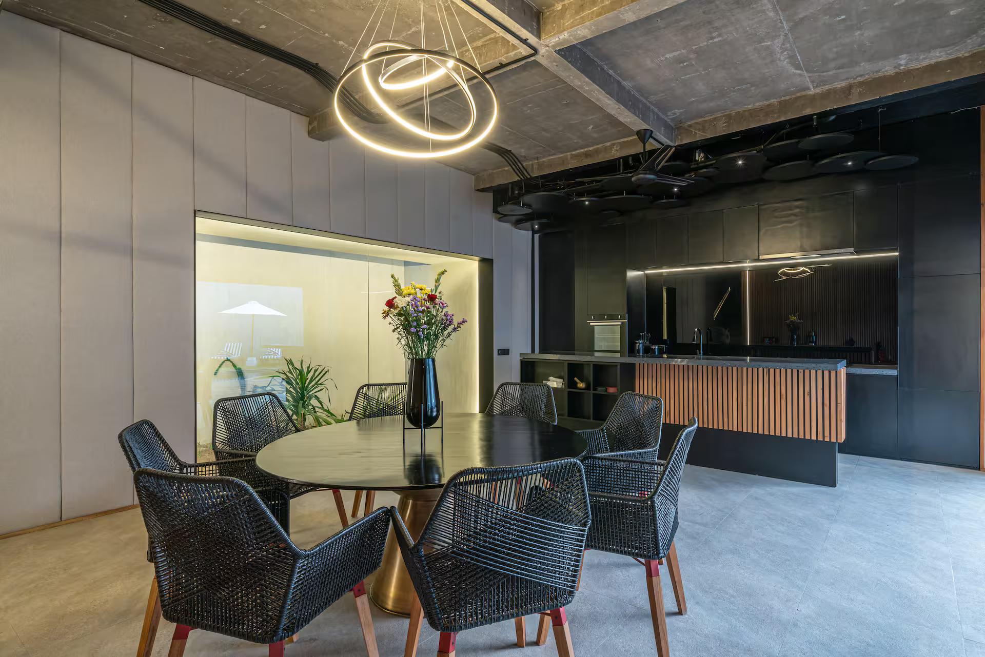Circular dining table with woven chairs under a lit ring pendant
