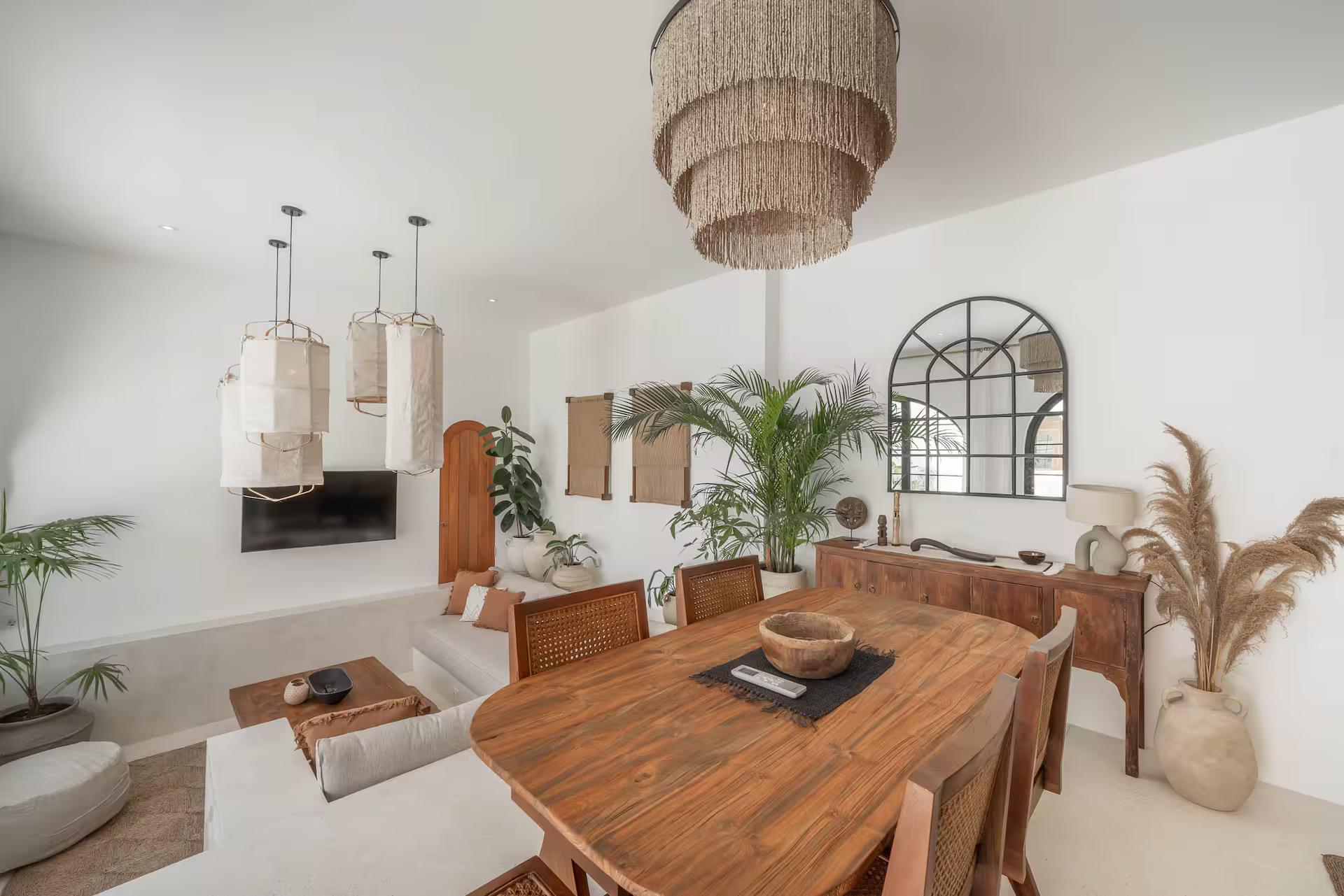Dining table and sectional under the raffia chandelier, arched window onto the courtyard