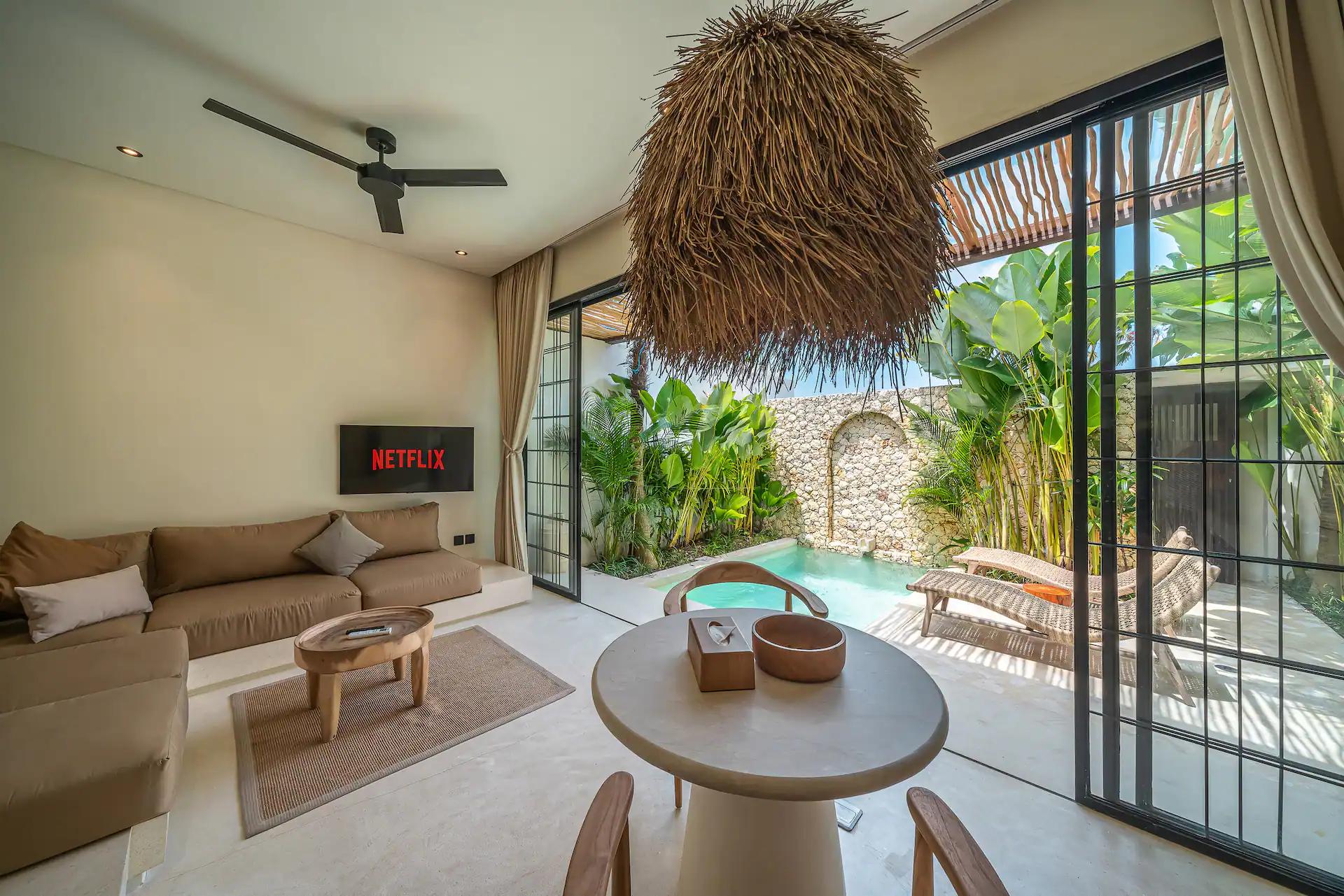 Round dining table under a shaggy reed pendant at Villa Lumma 3, the pool through the glass
