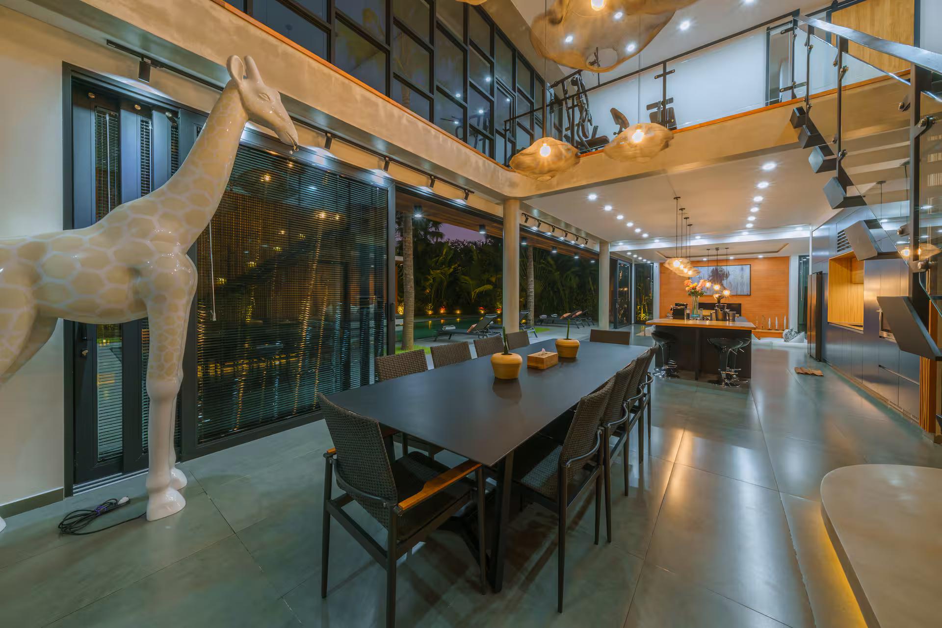 Black dining table for ten under blown-glass pendants beside a life-size giraffe