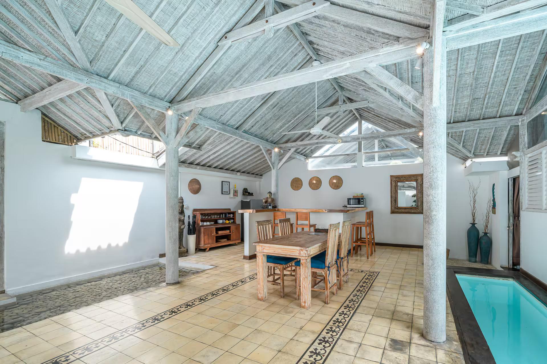 Dining table for six in the open pavilion, pool edge visible past the timber posts