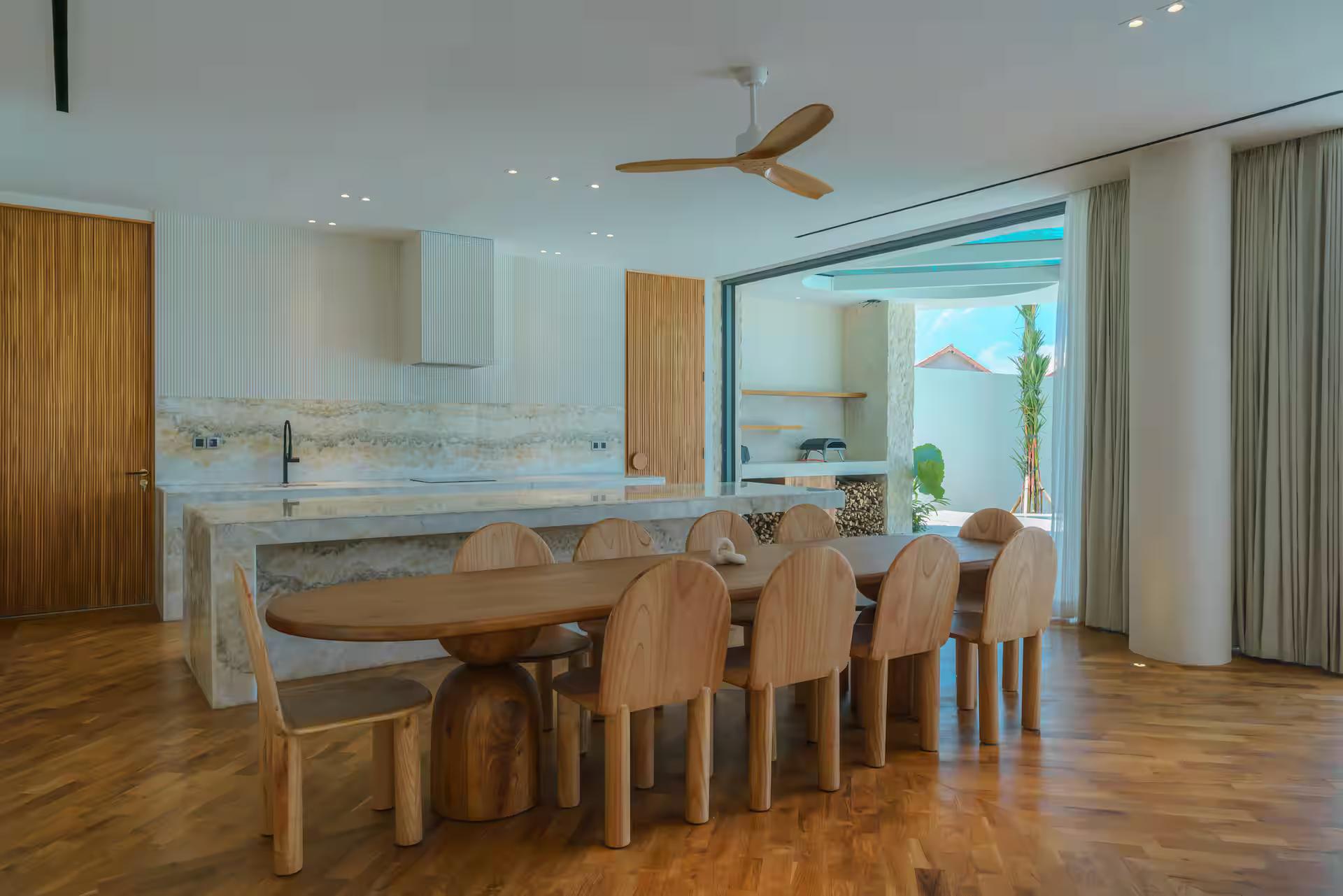 Long timber dining table for sixteen beside Villa Babylon's veined marble kitchen bar