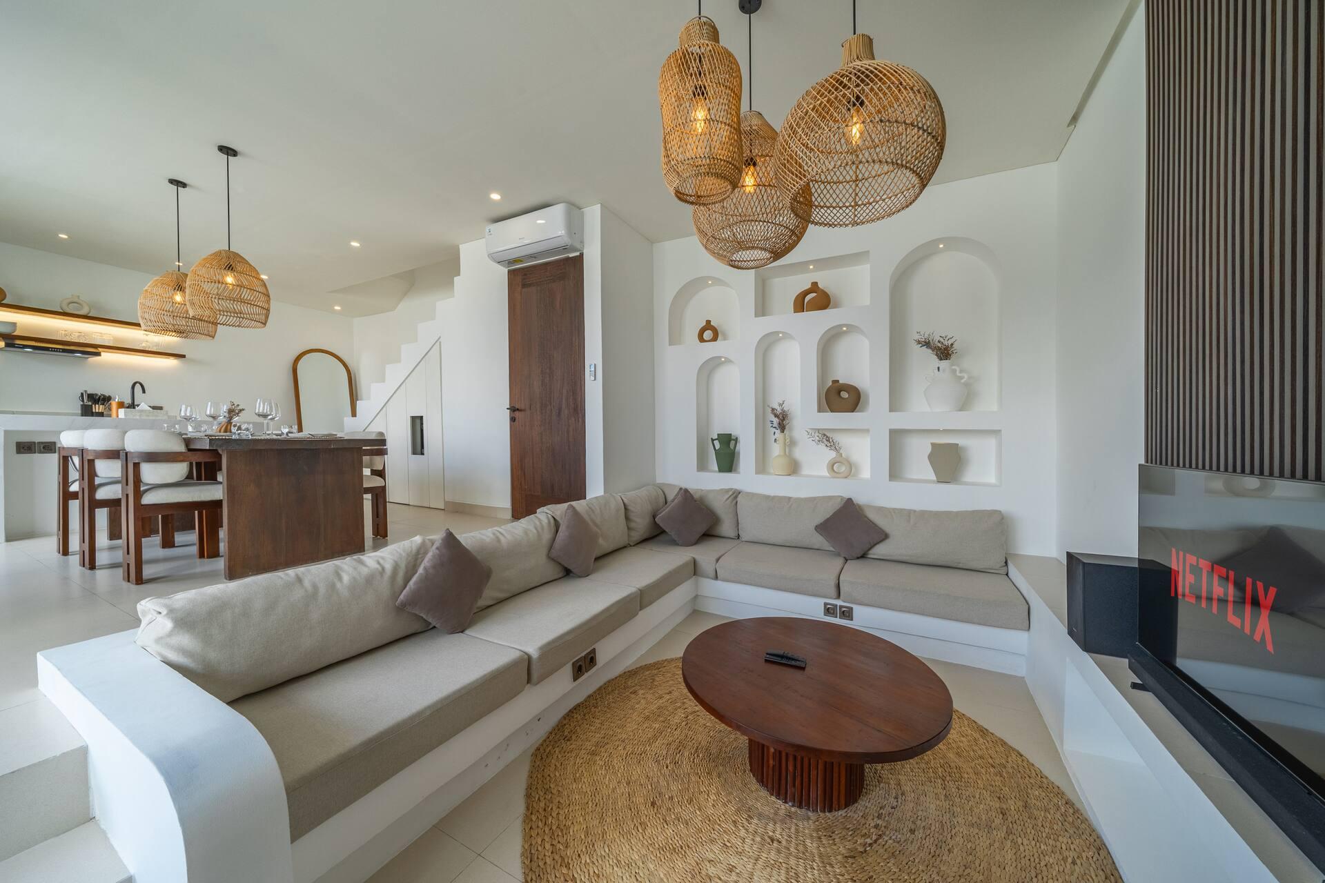 Built-in plaster banquette seating around a round timber table, with arched display niches and rattan pendants overhead