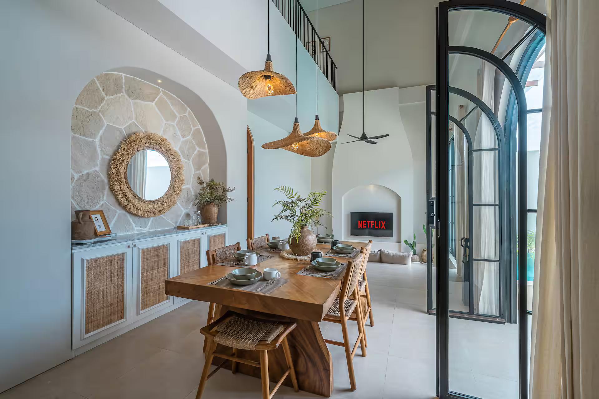 Dining table and rattan chairs beneath a round mirror framed in crazy paving