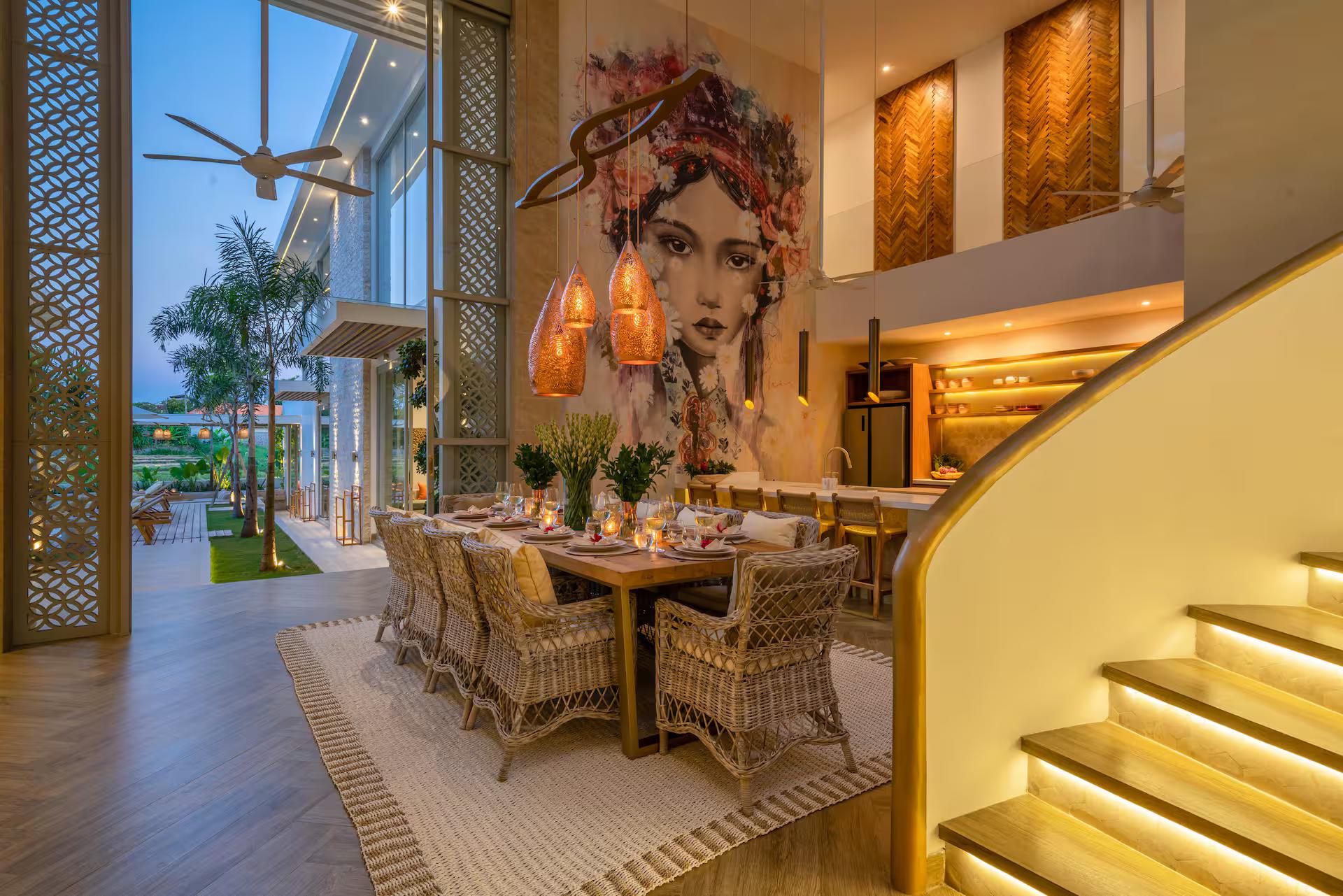 Dining table under woven pendants, the mural and the curving staircase behind at Villa Vida