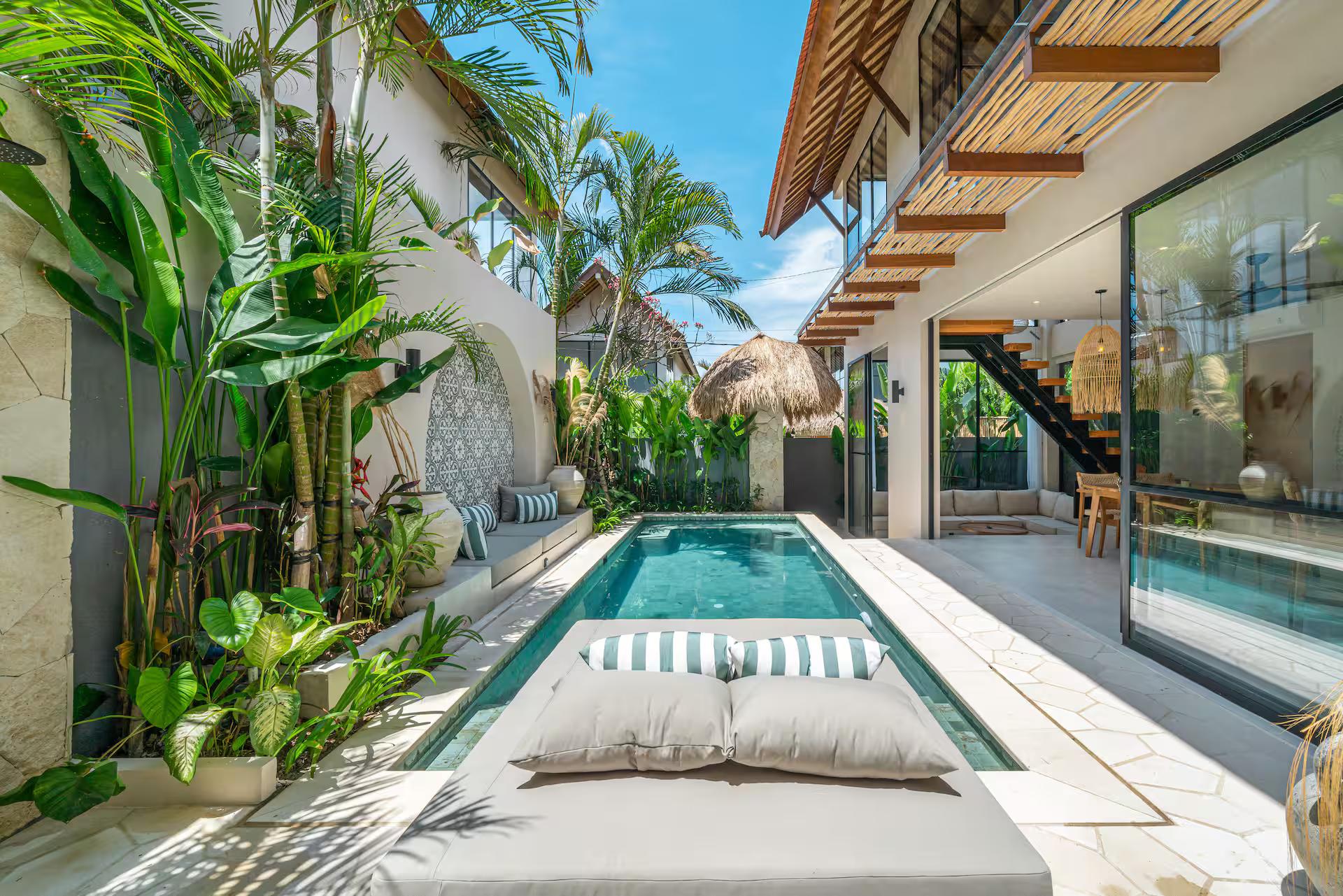 The narrow pool seen from the far end, palms and thatched parasols along the courtyard wall