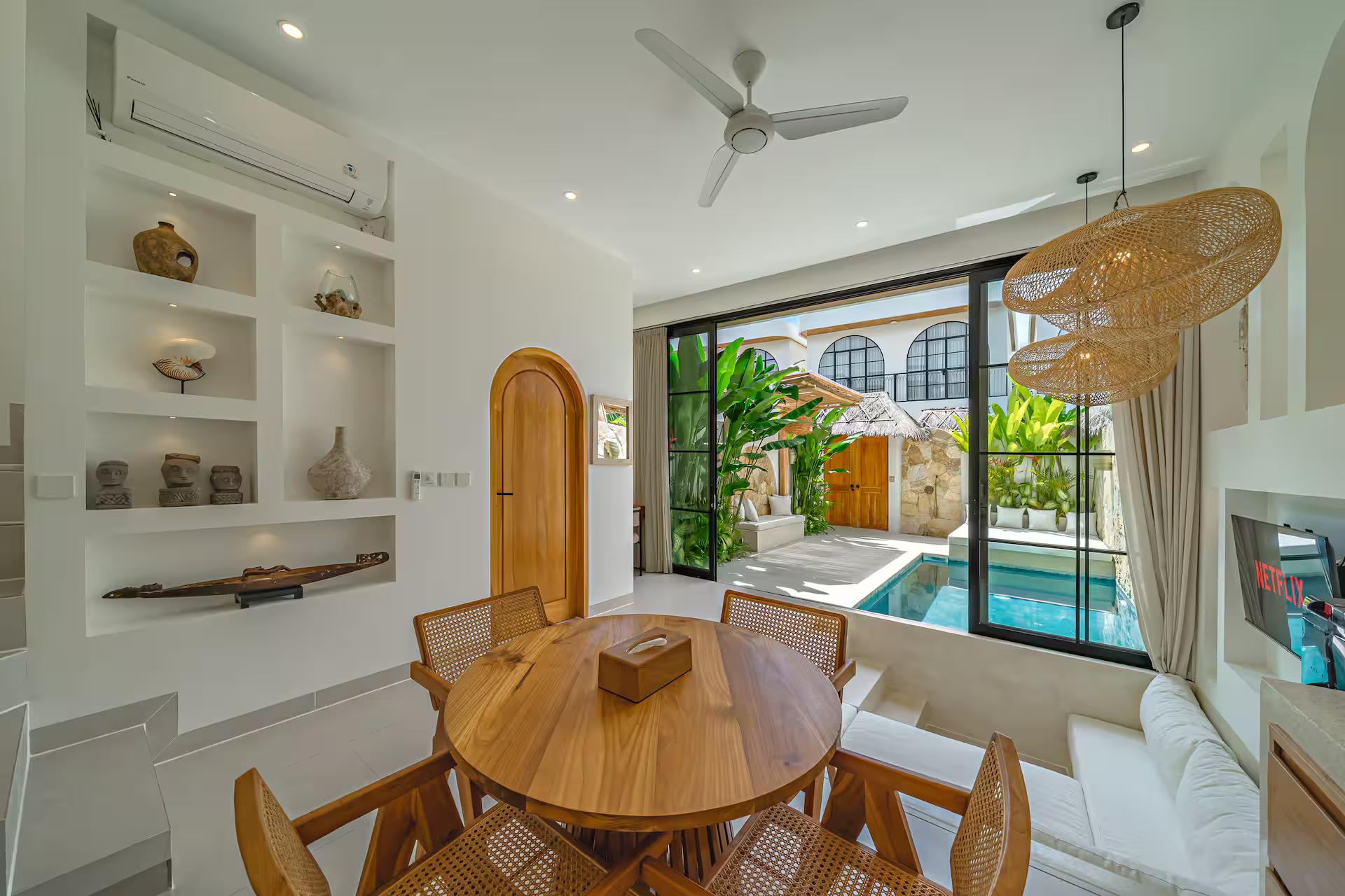 Round timber dining table and cane-backed chairs beside the arched courtyard door