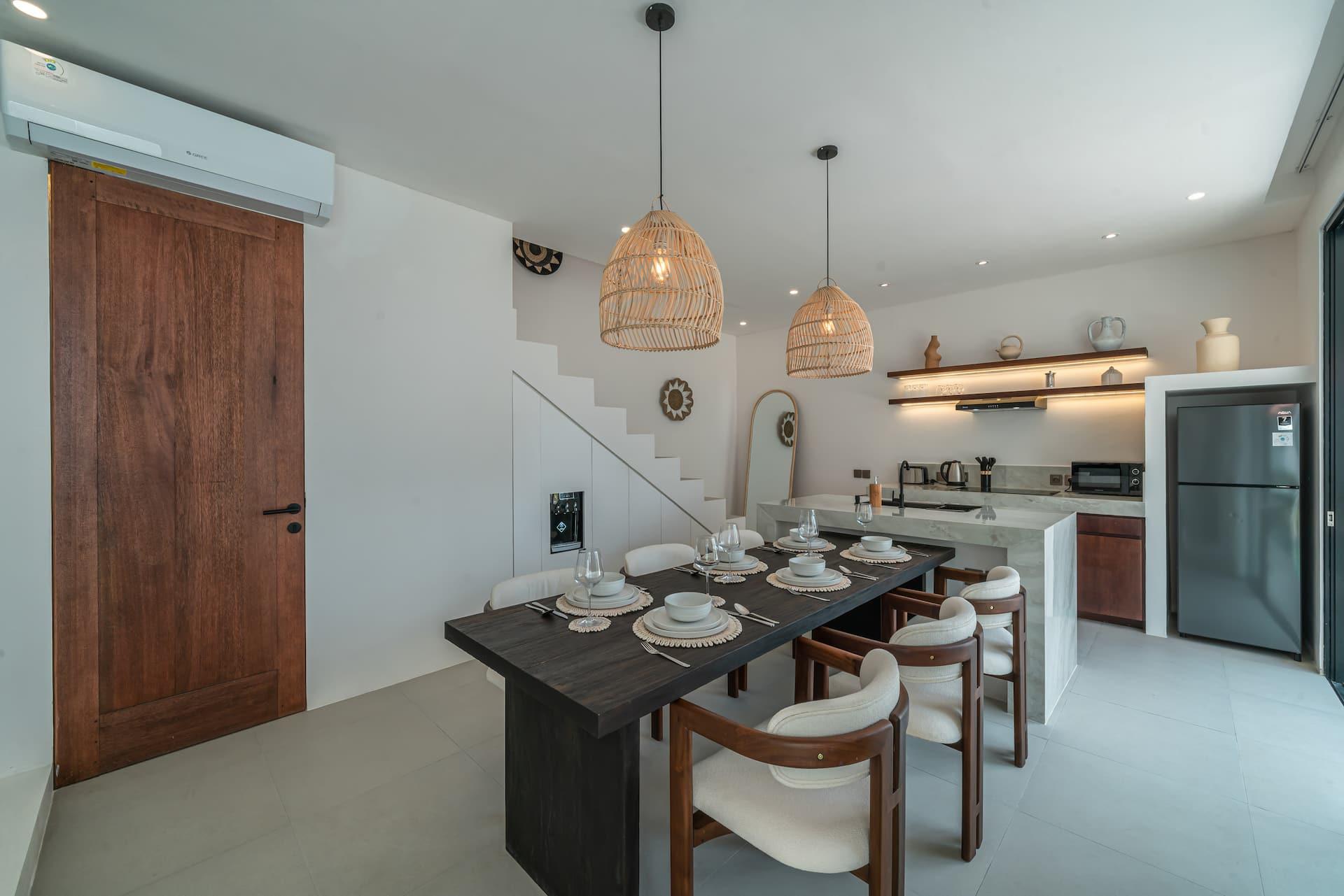 Dark timber dining table laid for six with cream upholstered chairs, beside the kitchen and staircase