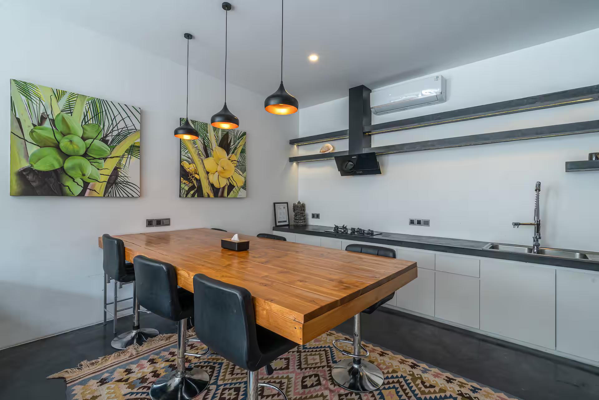 Timber dining table and black stools below the kitchen's green botanical canvases