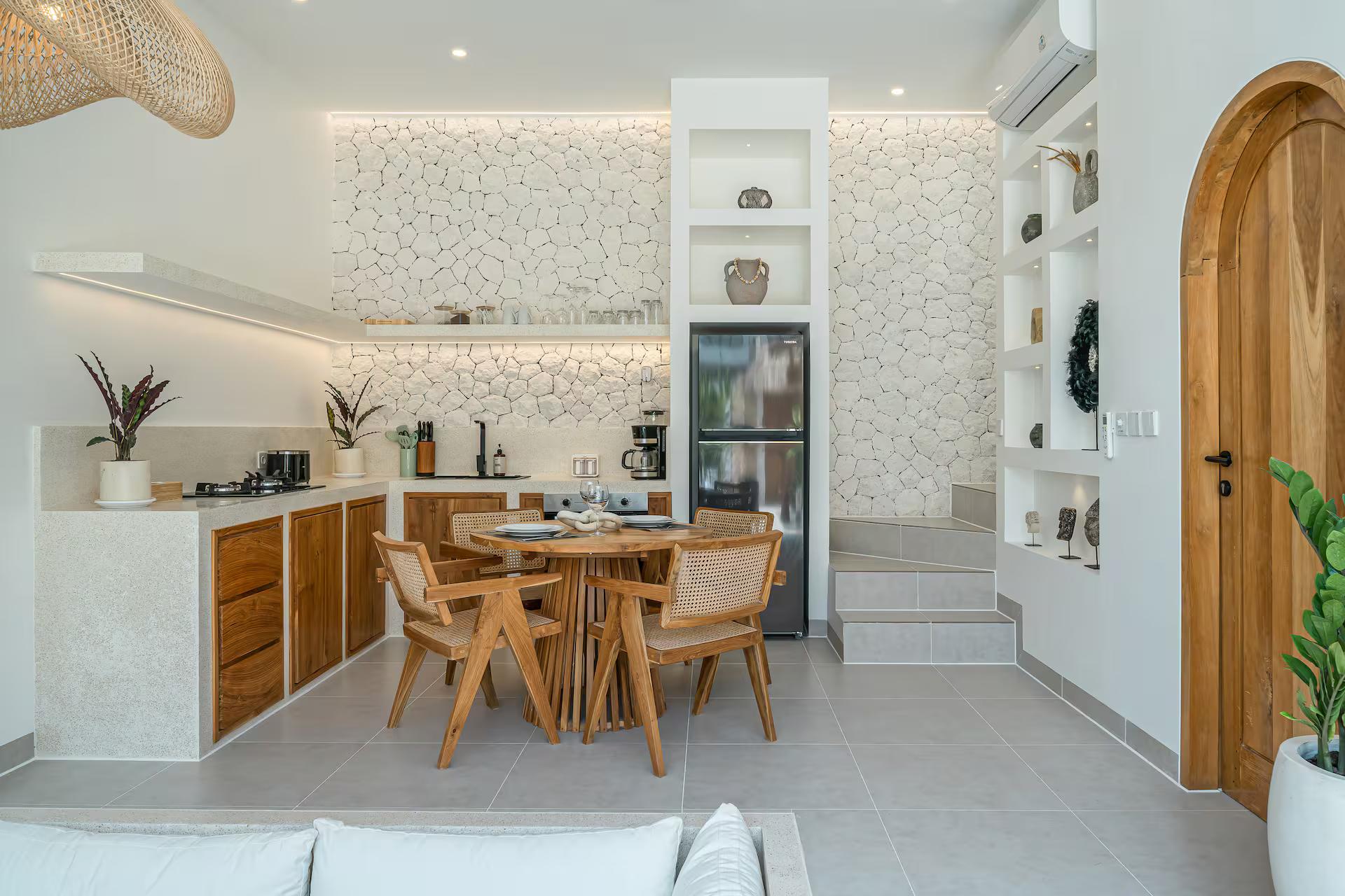 Round timber dining table and cane chairs beside the timber kitchen and stone splashback