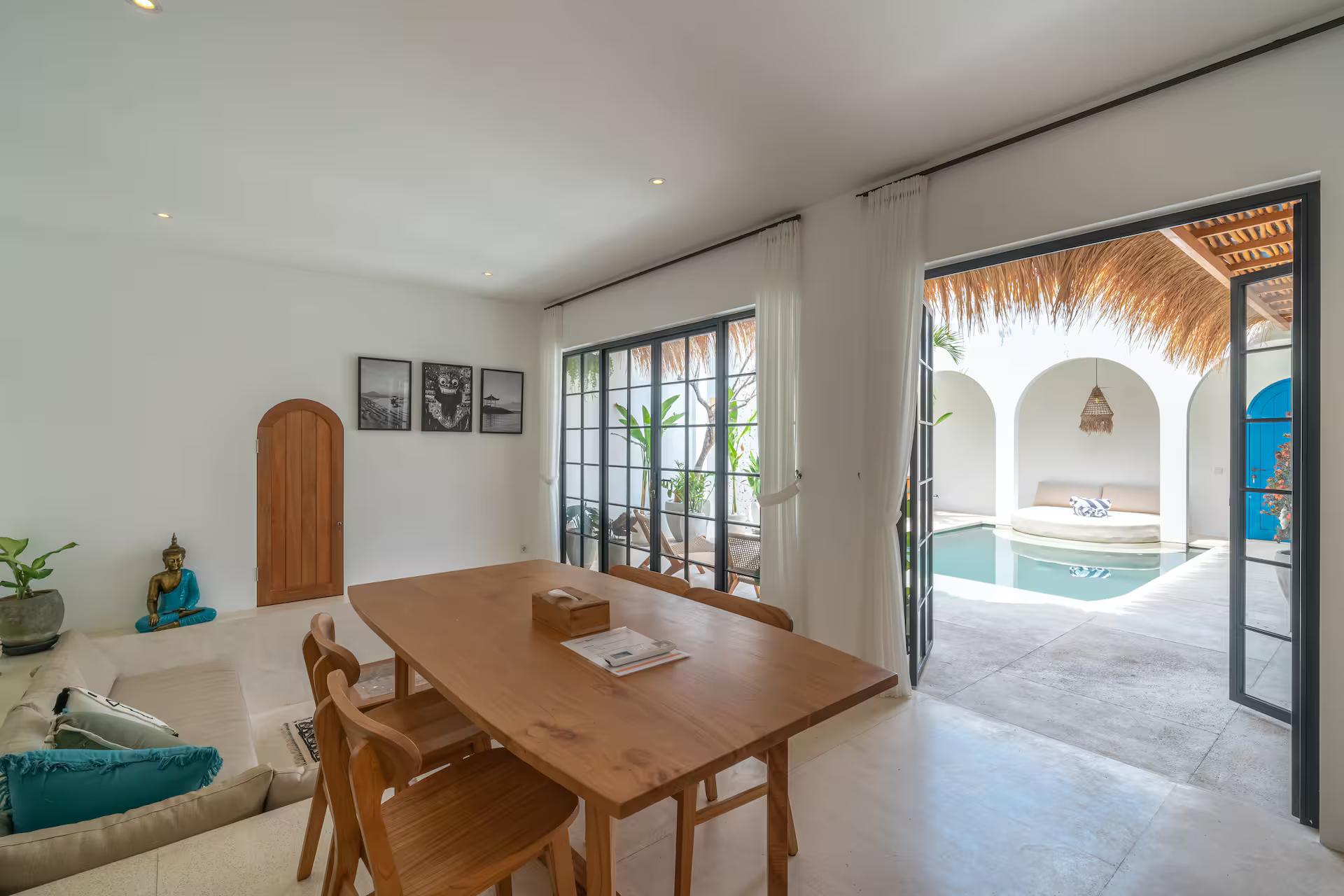 Long teak dining table and cane chairs, glass doors open to the courtyard pool