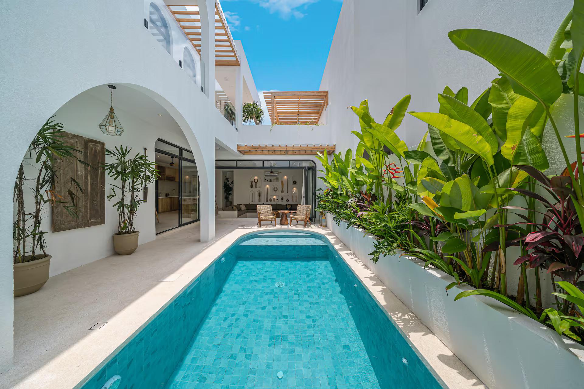 Pale-tiled lap pool seen the length of the courtyard, arches and heliconia along one wall