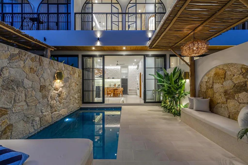 The pool at Villa Shams after dark, limestone wall lit and the living room glowing