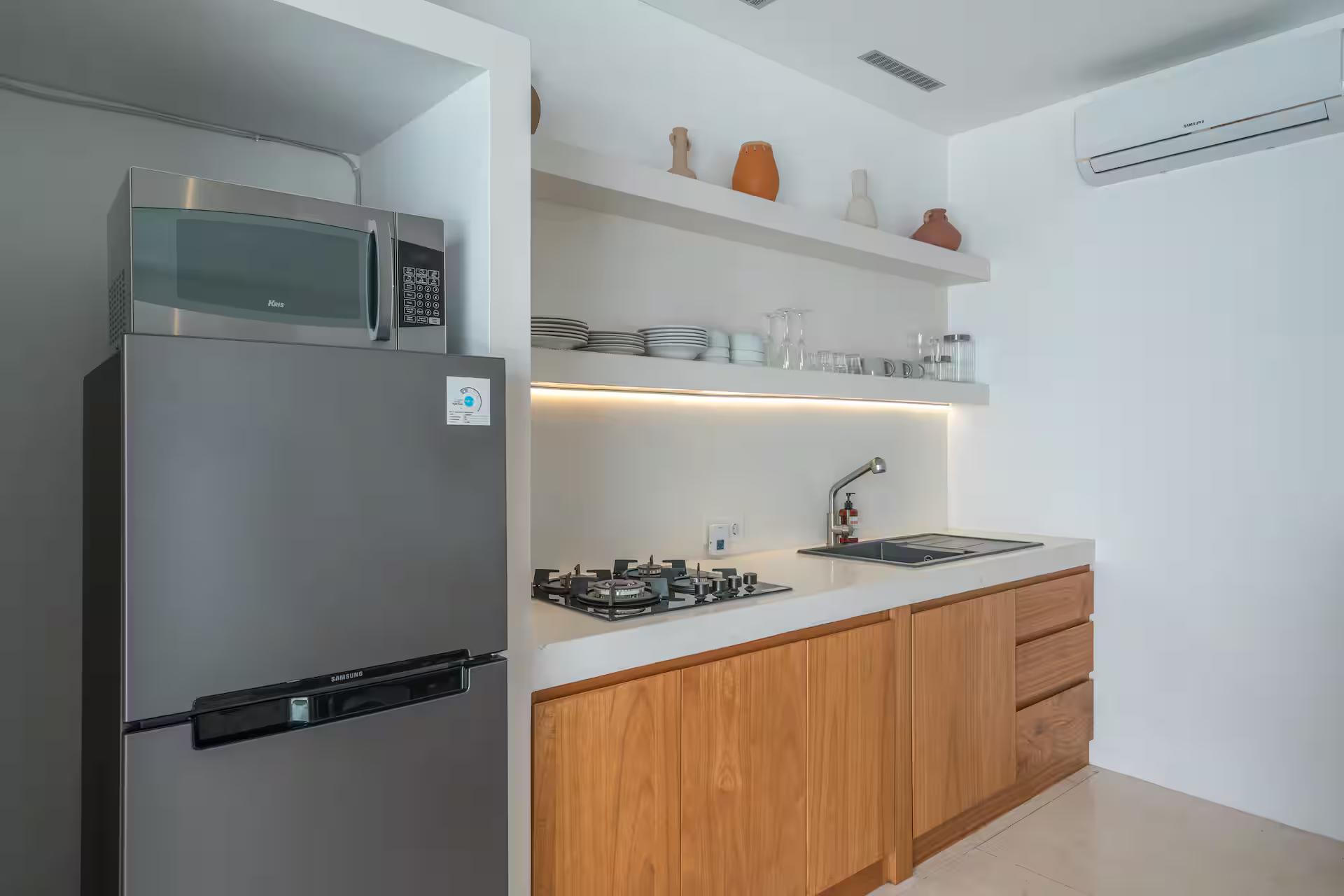 Teak kitchen with white stone counters, gas stove and lit open shelving