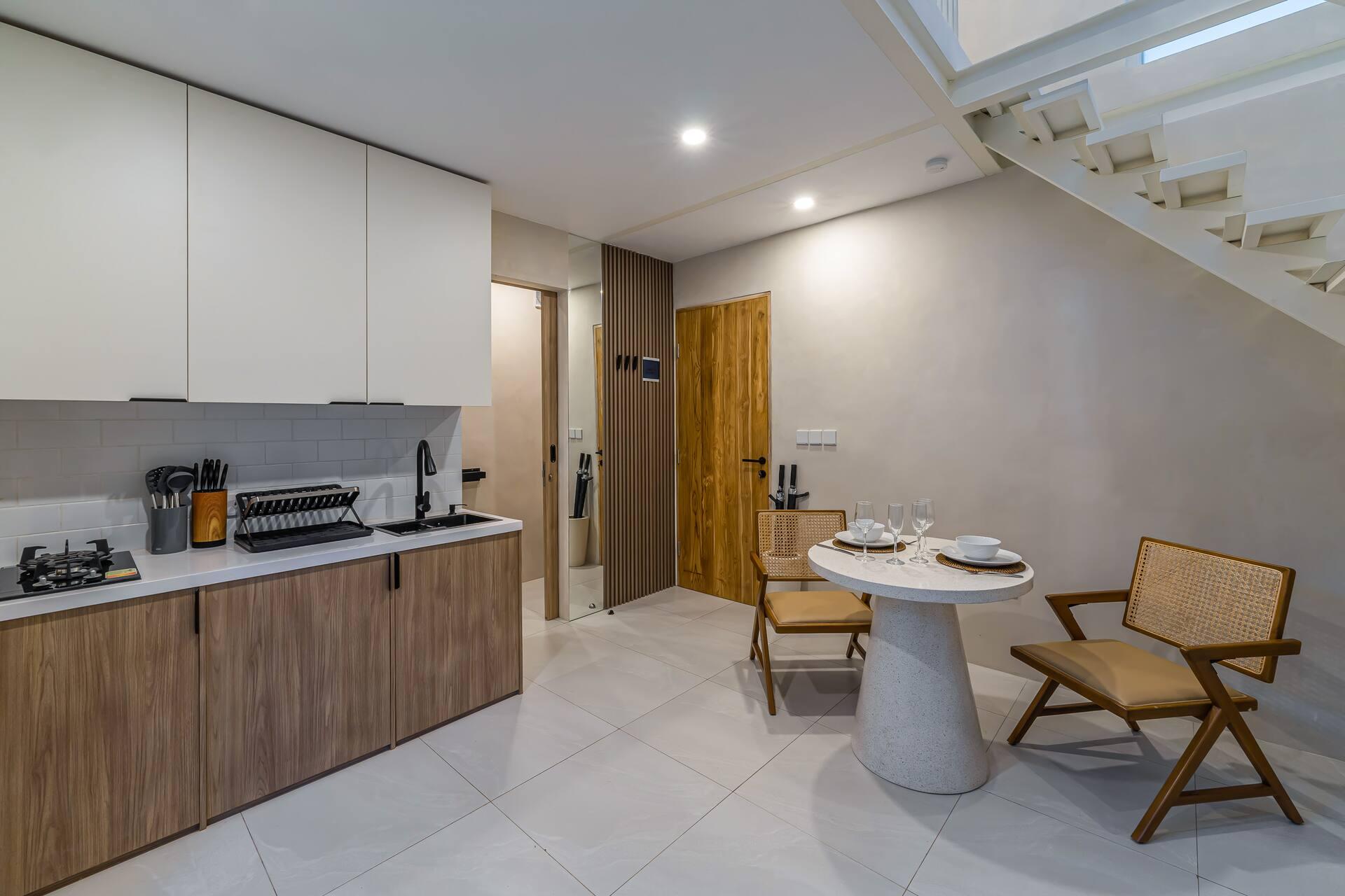 Kitchenette counter in pale timber with a stovetop, beside the round dining table