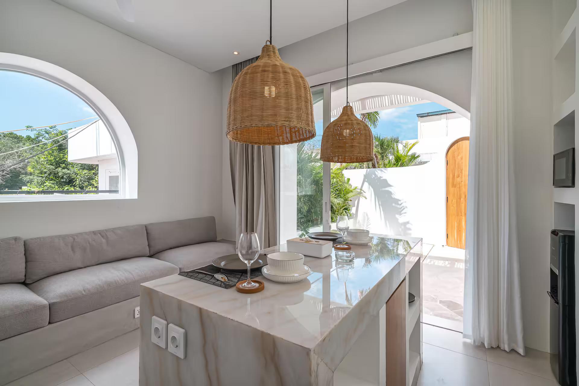 Banquette sofa and marble island beneath an arched window and rattan pendants