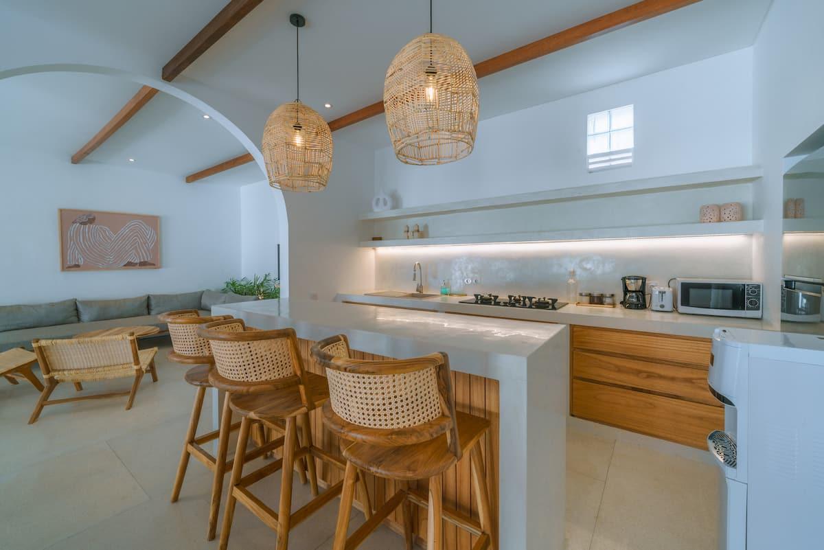 Kitchen island in slatted timber under a vaulted ceiling with exposed beams and rattan pendants