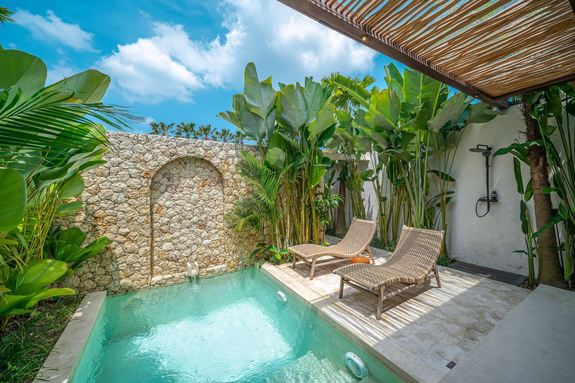 Aqua-tiled plunge pool against a coral-stone wall with a tall arched niche, palms crowding in