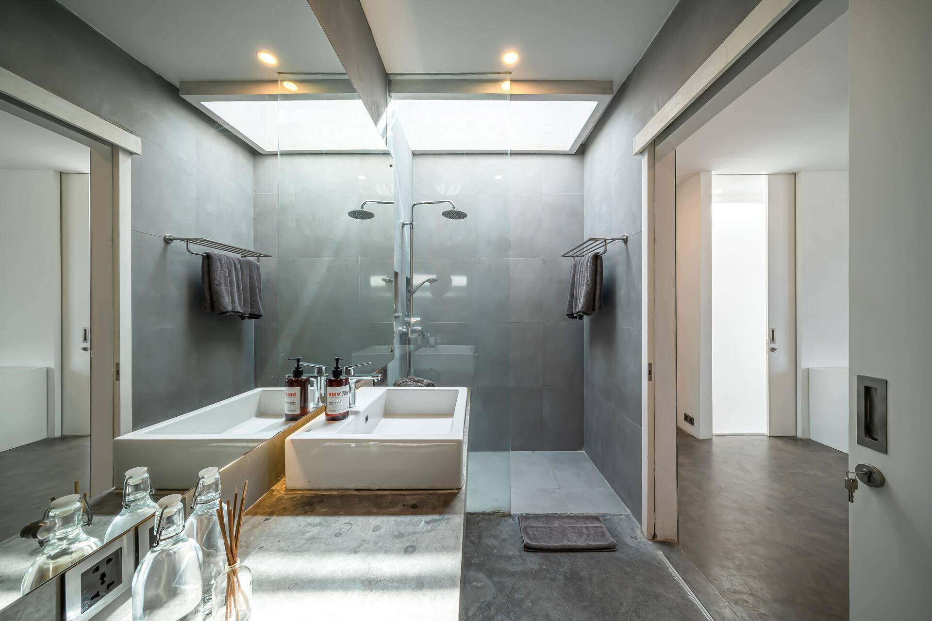 Grey microcement bathroom with a twin-head walk-in shower and a slot skylight