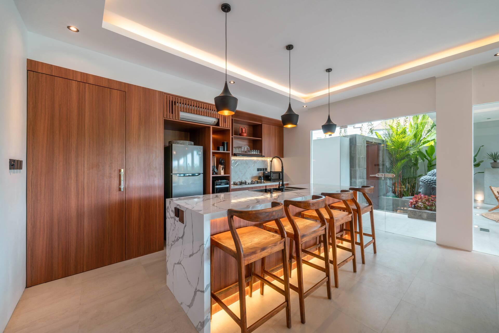 Stone-topped kitchen island with bar stools, warm light beneath the timber cabinets