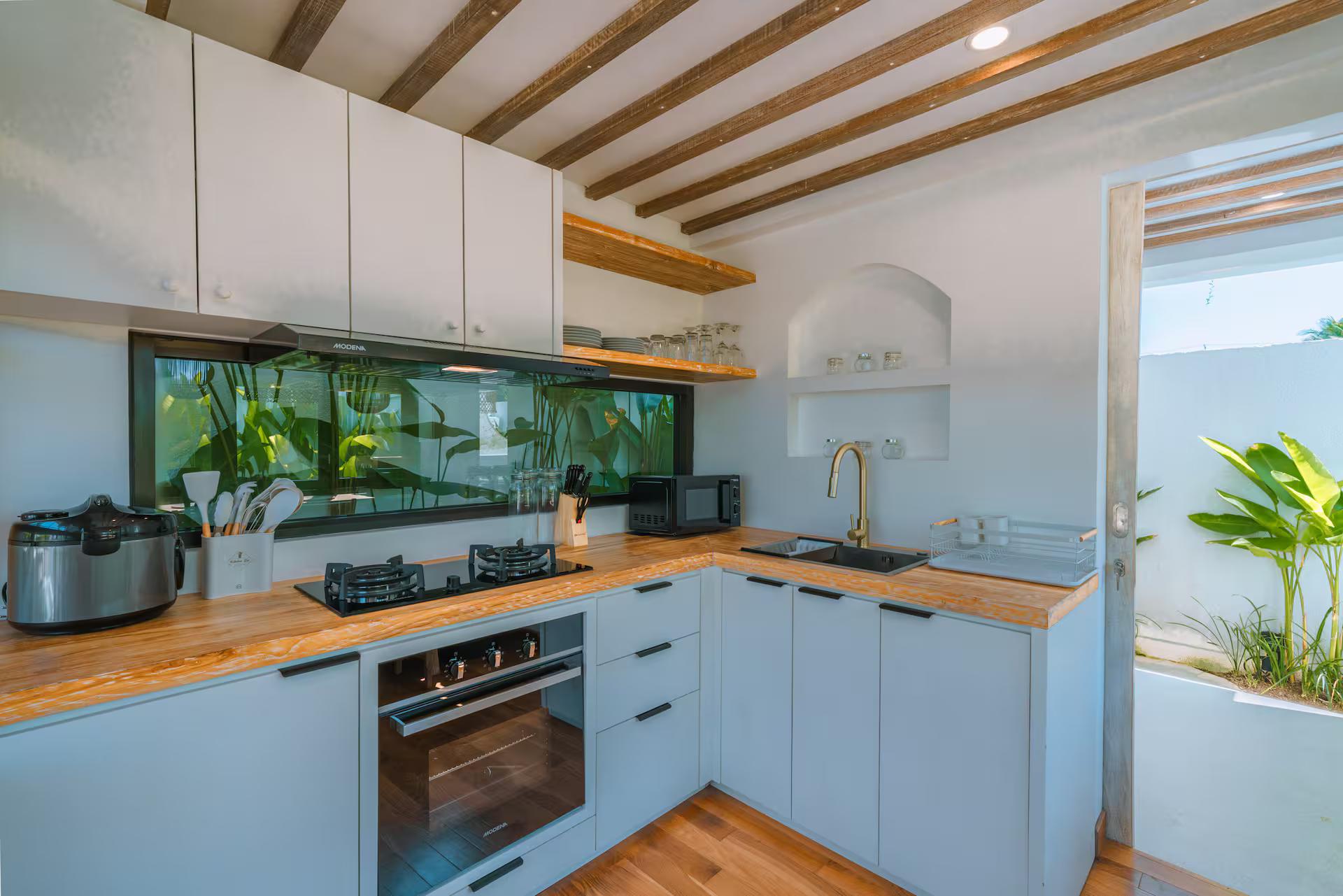L-shaped kitchen in white joinery with a timber worktop, oven and brass tap