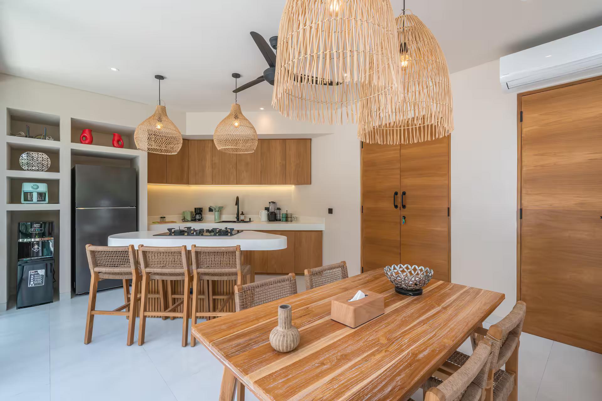 Teak dining table and curved kitchen island under two large fringed rattan pendants