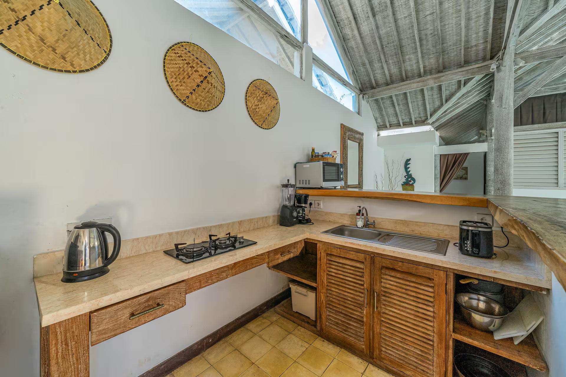 Kitchen with pale stone counters, louvred timber cupboards and woven fan discs on the wall
