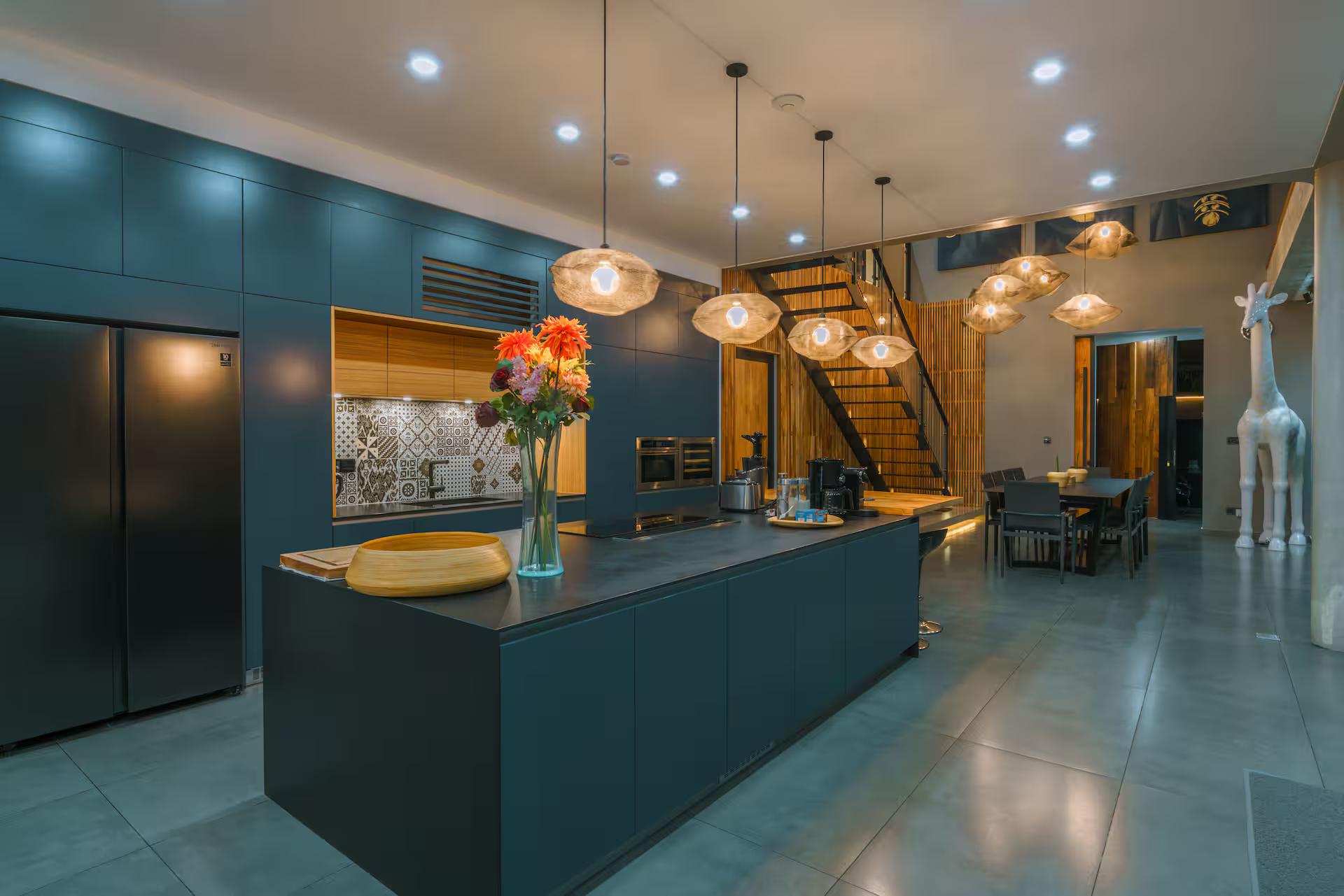 Deep blue kitchen joinery and island at Villa Aless, the staircase rising behind
