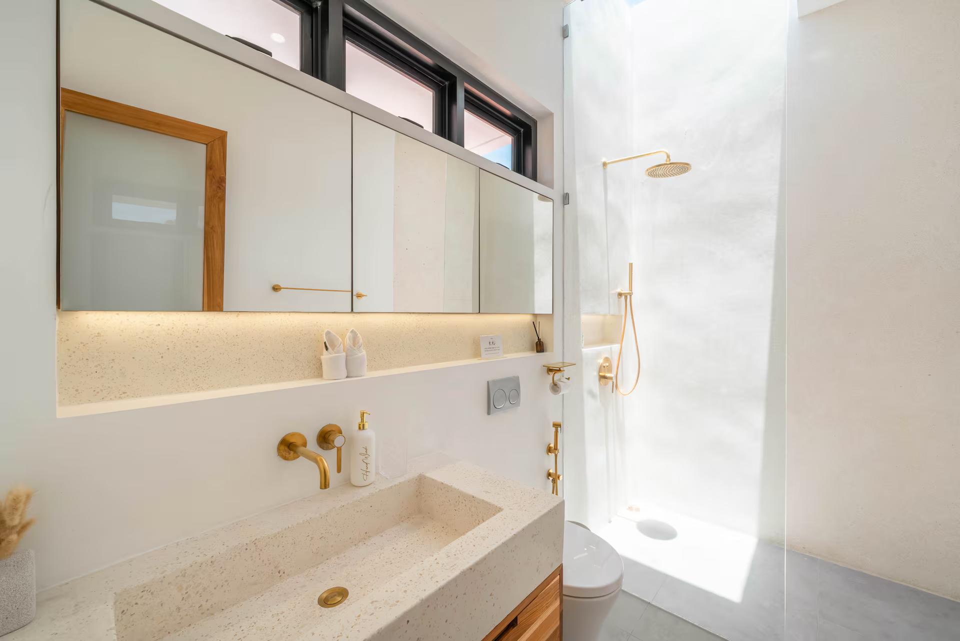 Terrazzo bathroom with a long trough basin, mirrored wall and brass tapware