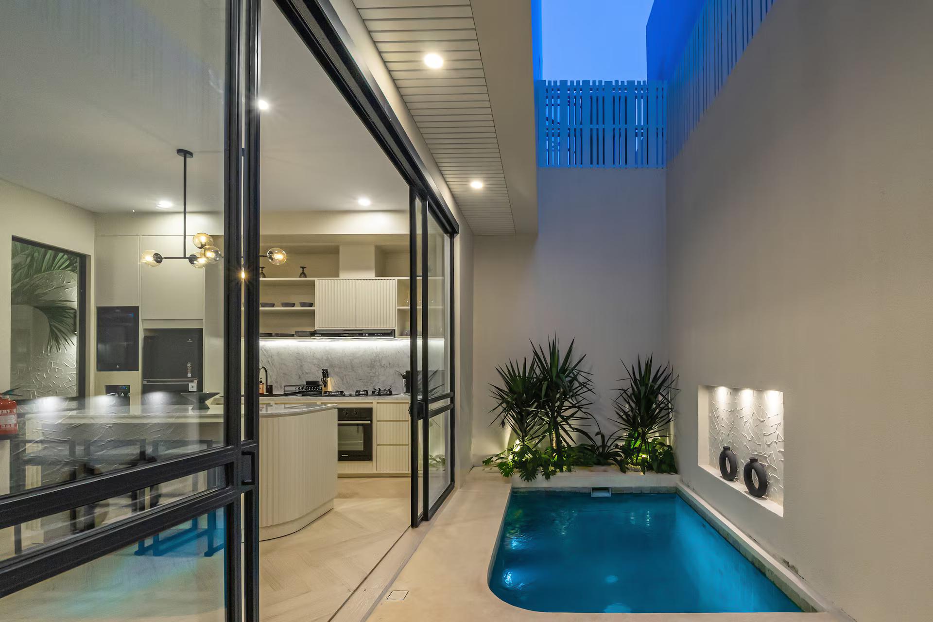 The pool court at Chandler Berawa after dark, lit niches cut into the render