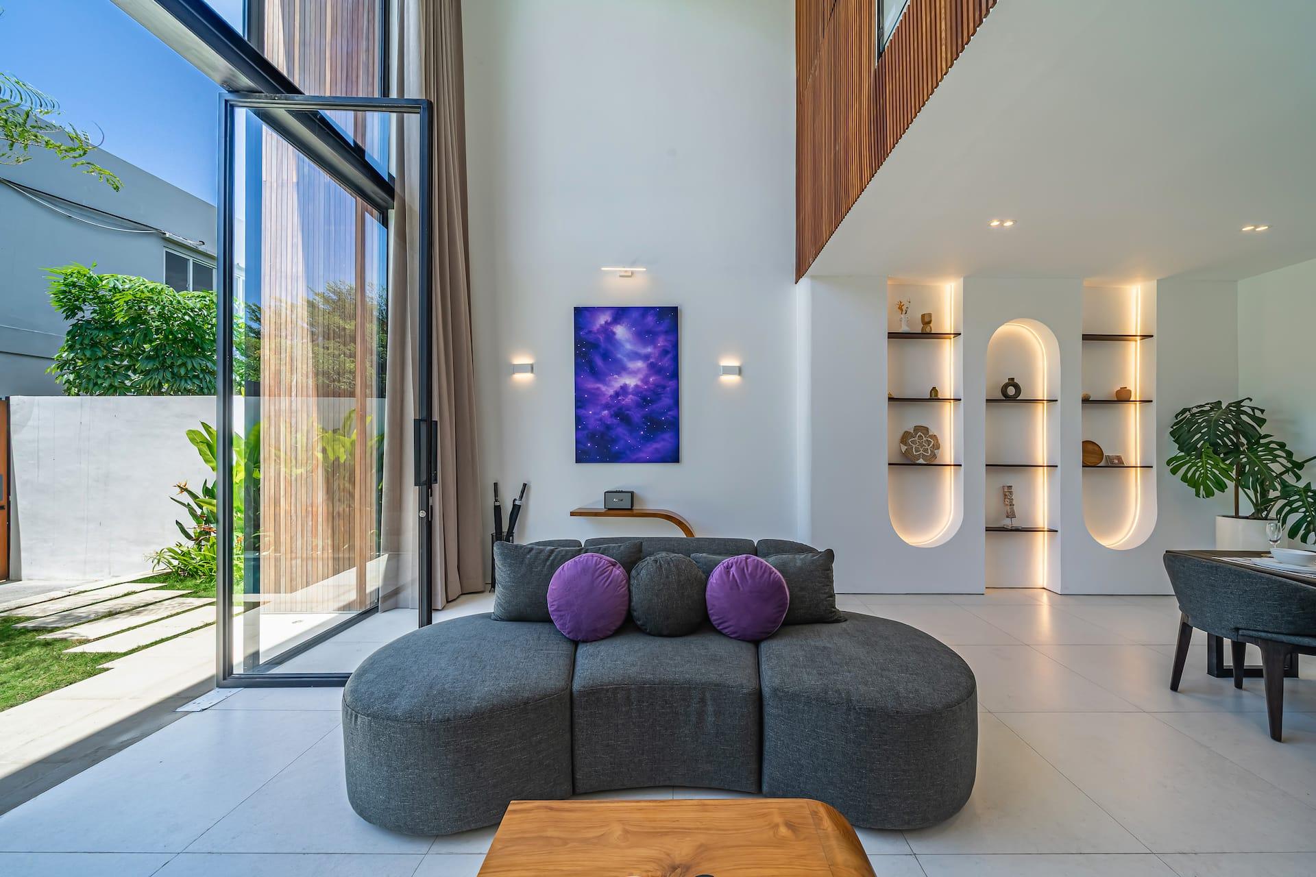 Curved grey sofa and live-edge timber table beside floor-to-ceiling glass opening onto the pool terrace