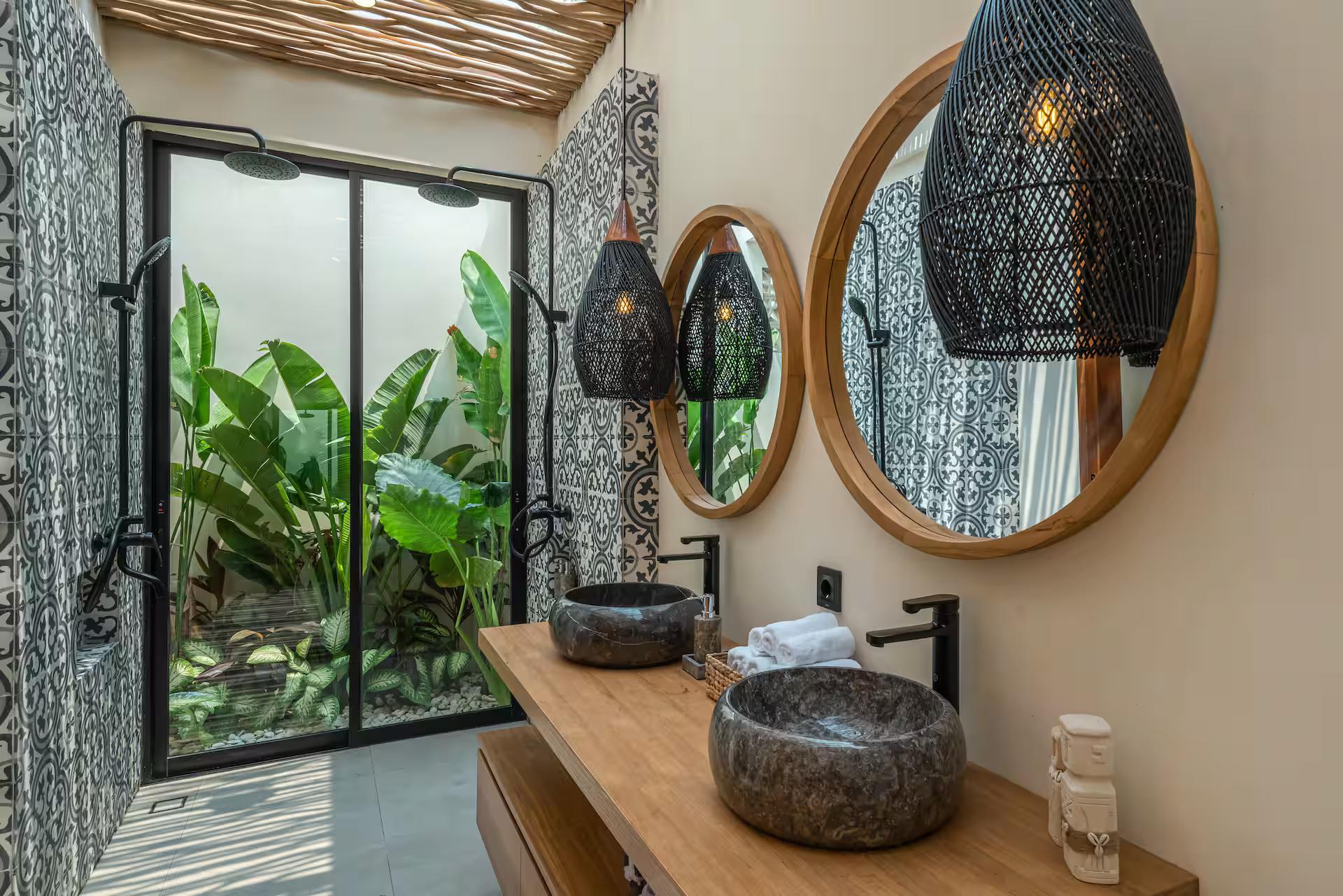 Twin black stone basins on a timber shelf beneath round rattan-framed mirrors