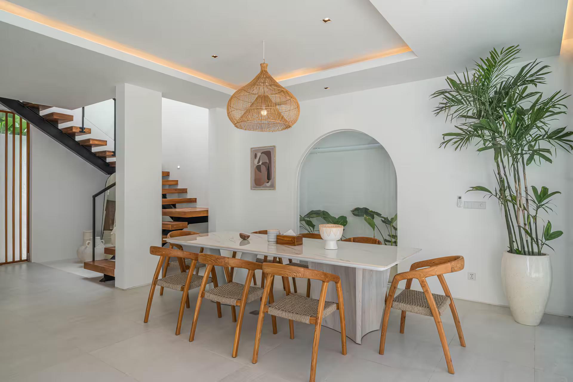 Marble dining table with timber chairs under a woven pendant, staircase rising behind
