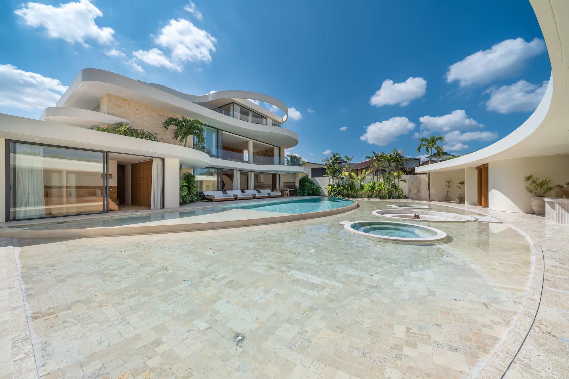 The pool and its circular jacuzzi under a bright sky, the villa's curved roof folding overhead