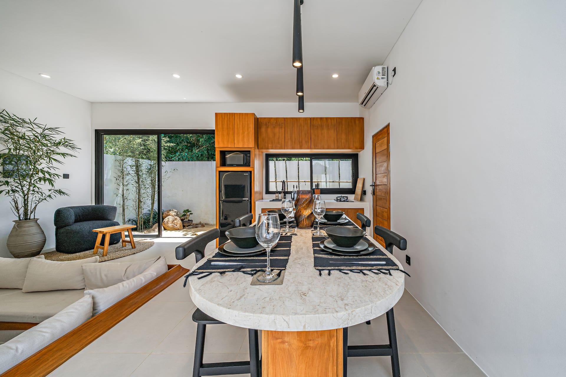 Pale stone dining table with black chairs and pendants, sunken lounge in the background