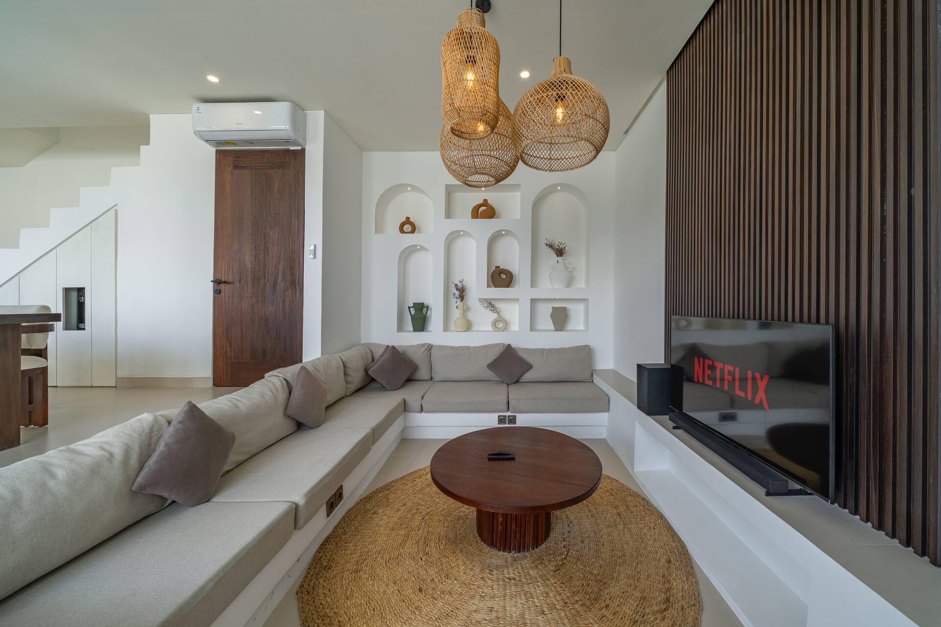A wall-mounted television on dark timber slats faces the L-shaped sofa and jute rug in the living room