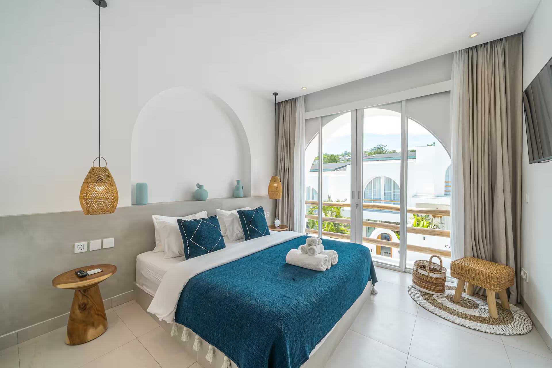 Second king bedroom with an arched window, teal throw and a carved timber side table