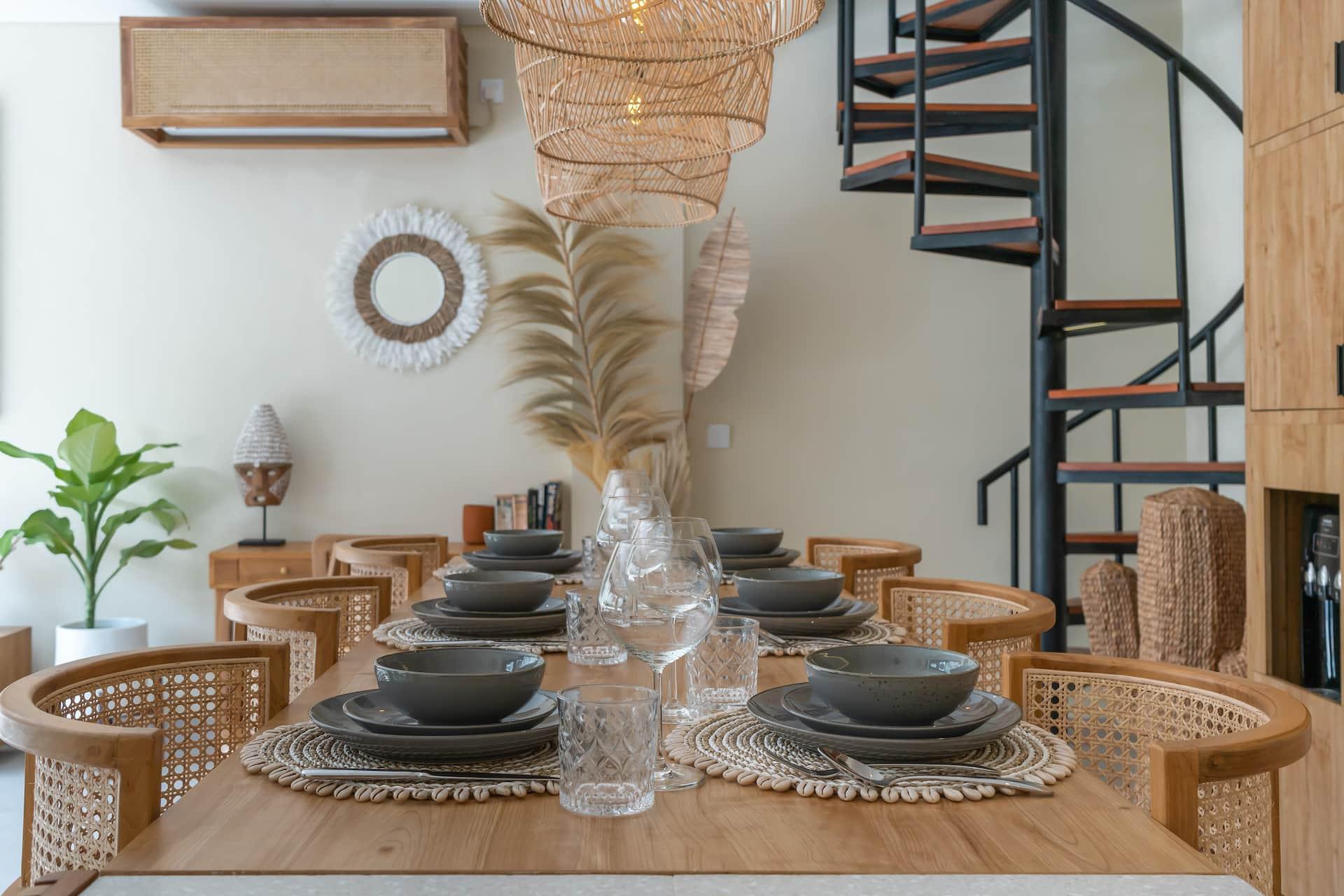 Timber dining table laid for six with cane chairs under woven rattan pendants