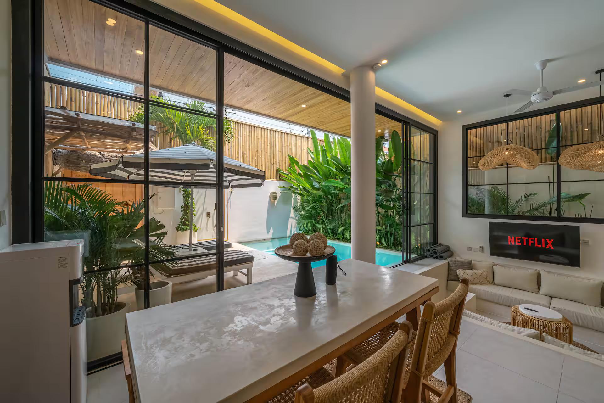 Dining table beside the black-framed glass wall, with the pool deck just outside
