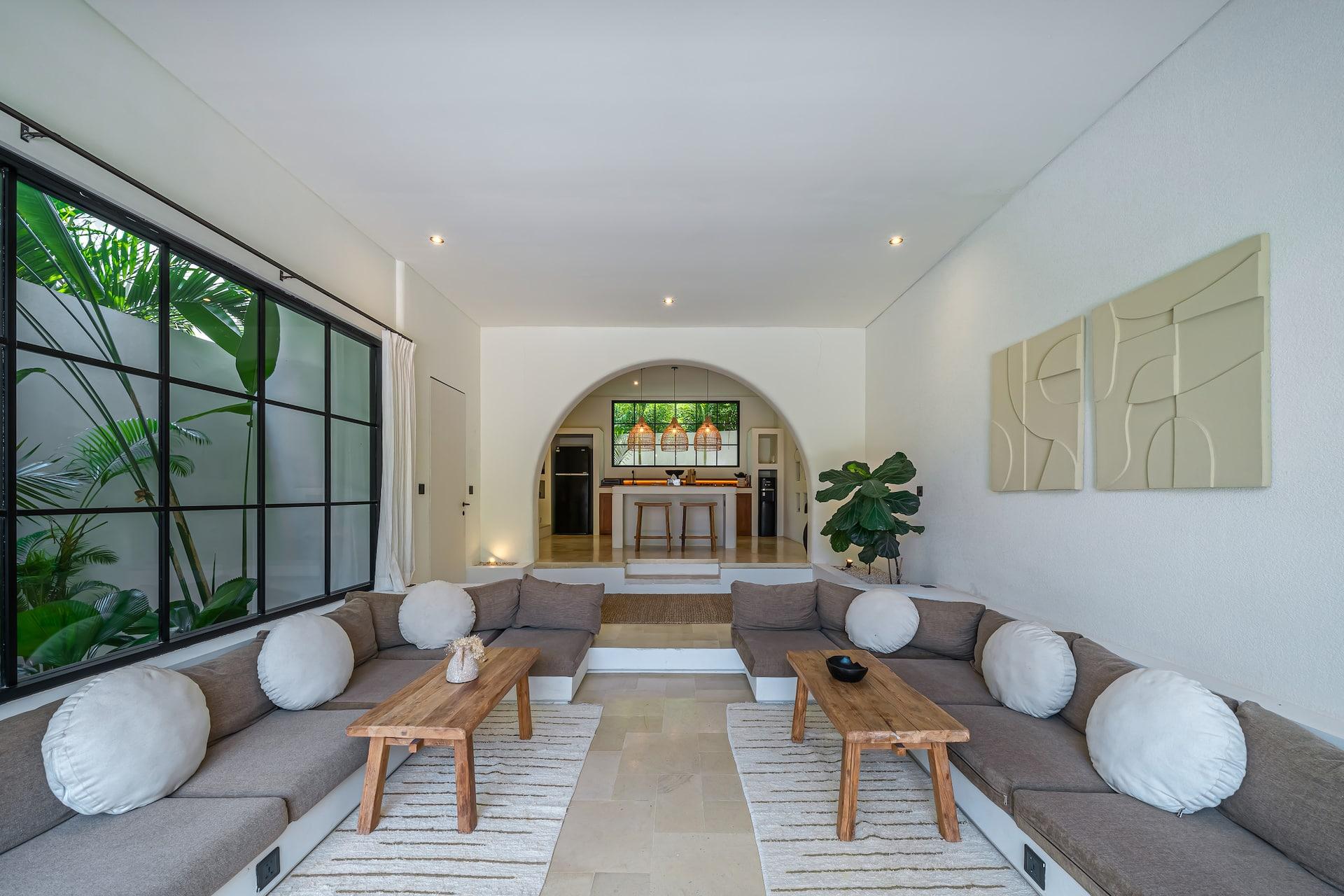 Built-in lounge seating with round cushions arranged around two timber coffee tables under a high white ceiling