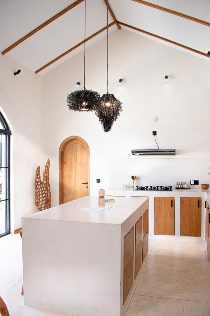 Pale concrete kitchen island with bar seating and a black fringed pendant overhead