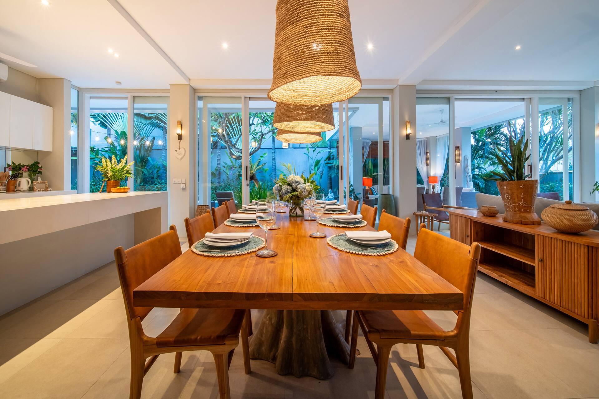 Villa Sunsara 2 dining room with warm teak chairs, a long table and glass doors to the pool garden