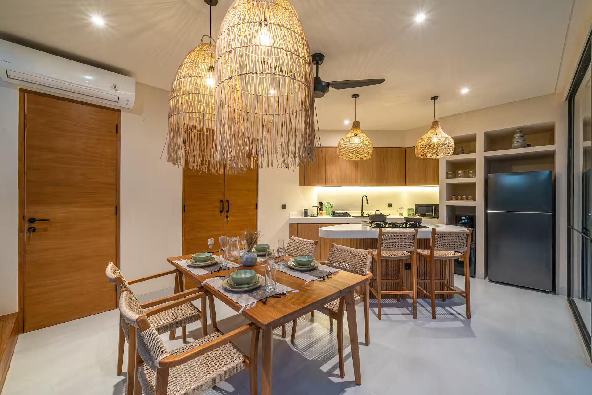 Dining table laid for six under fringed rattan pendants, with the kitchen beyond