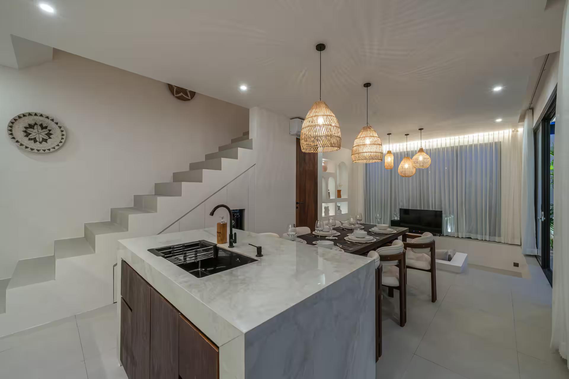 Kitchen island in dark timber with a thick white marble top and integrated hob