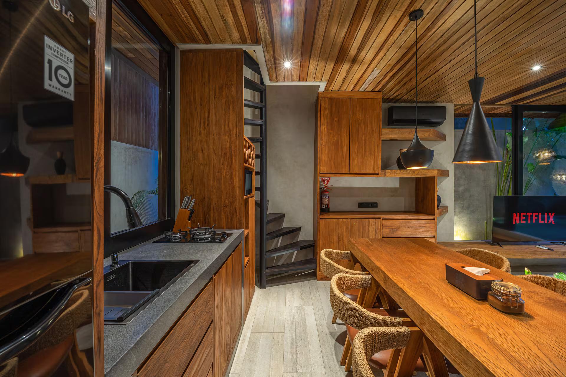 Kitchen in timber cabinetry with a stone counter, slatted wine rack and black cone pendants