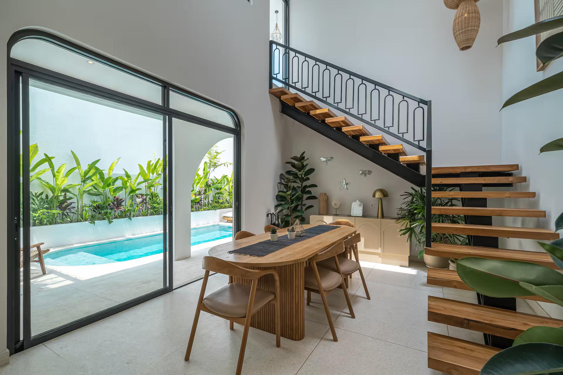 Dining table for six beside the open-tread timber staircase, glass doors framing the pool