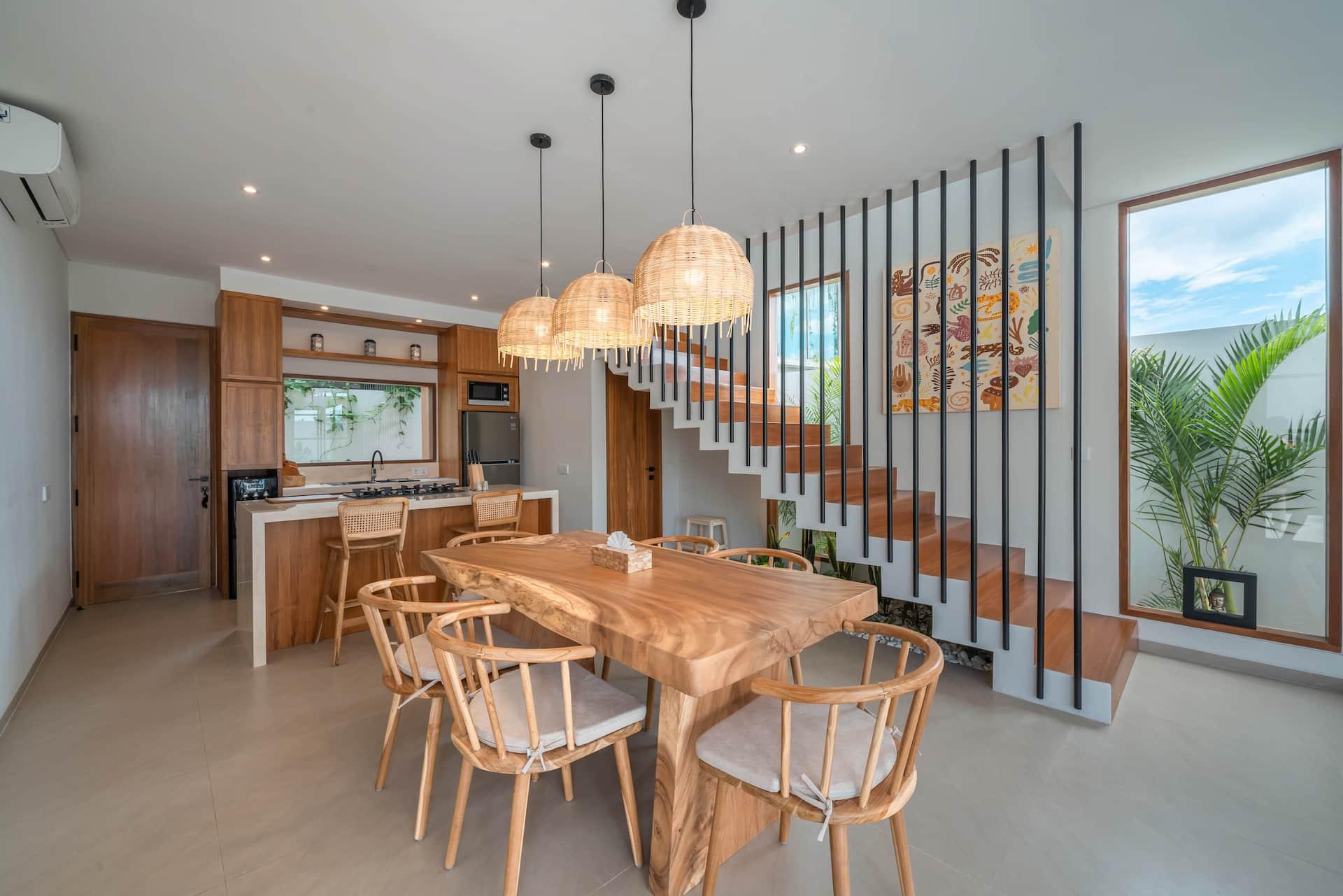 Dining area at Villa LouLou: live-edge timber table under rattan pendants beside the floating staircase