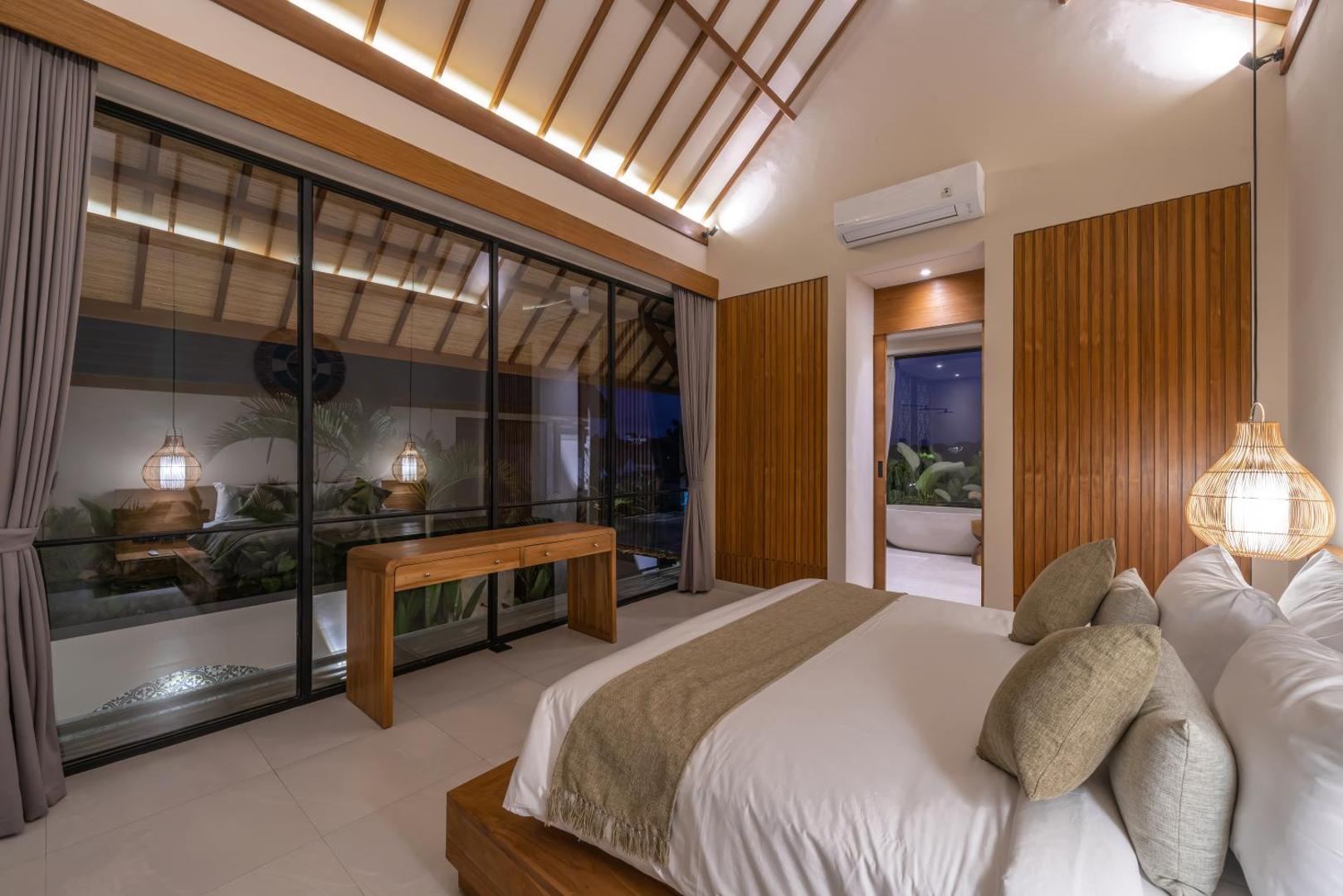 Bedroom looking out through full-height glass to the pool terrace at Villa Nalaka
