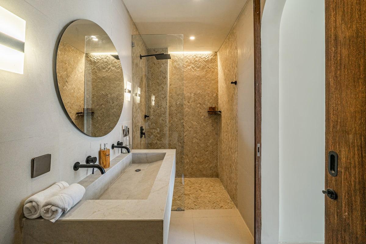 En-suite with a carved stone trough basin and a walk-in shower lined in herringbone mosaic