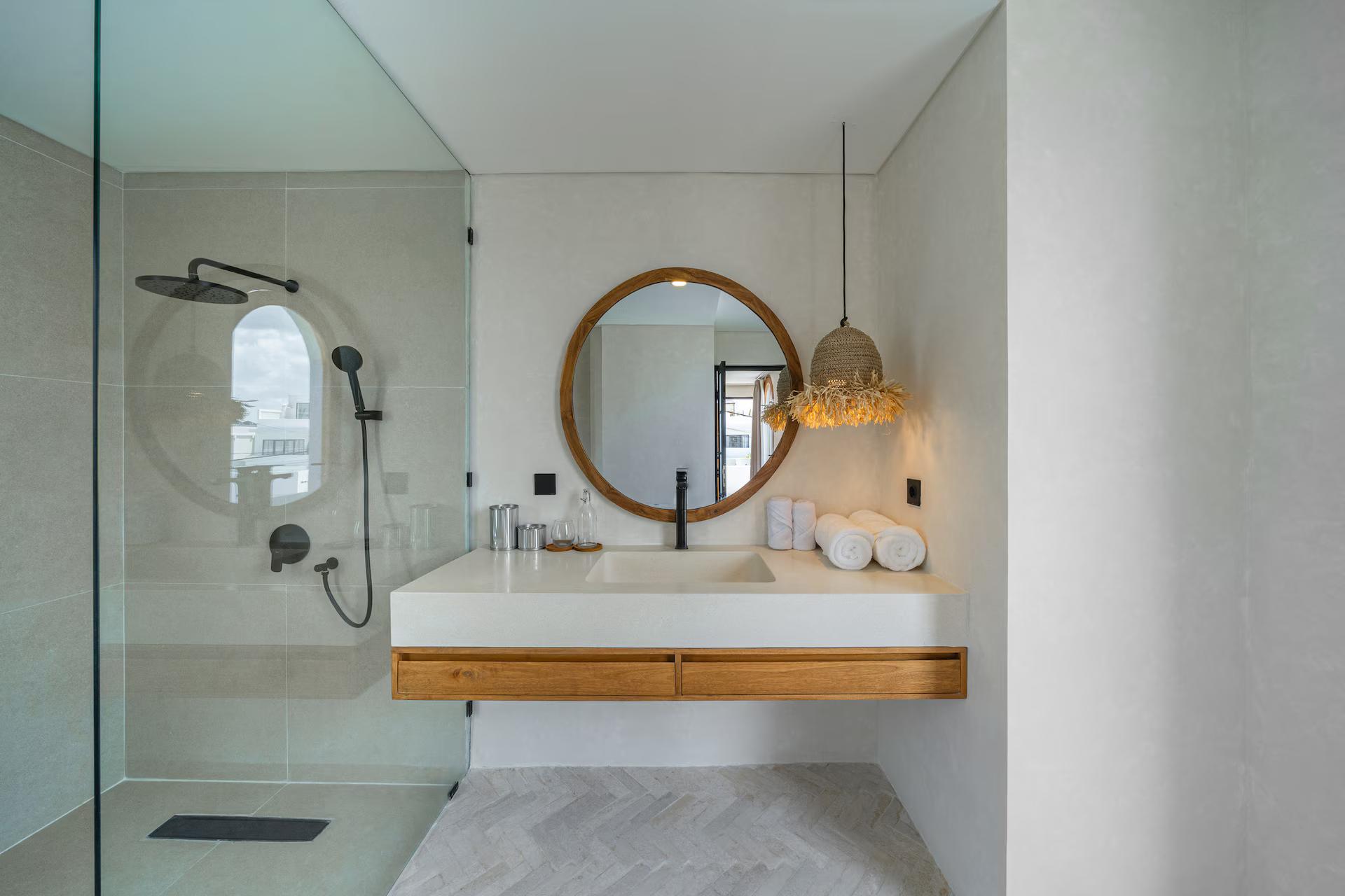 En-suite at Villa Terra Calma with a walk-in glass shower, round timber mirror and a raffia pendant
